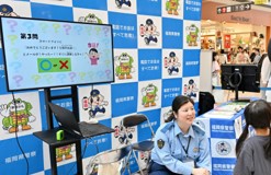 福岡県警察のブースで詐欺など防犯に関するクイズの問題が書かれた画面を見る子供と回答を待つ警察職員の様子