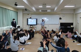 財政に関するクイズを出す講師と挙手にて回答する児童の様子