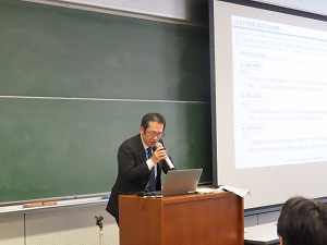 スクリーンに資料が映しながら教室の前で講師がマイクを使って説明している様子