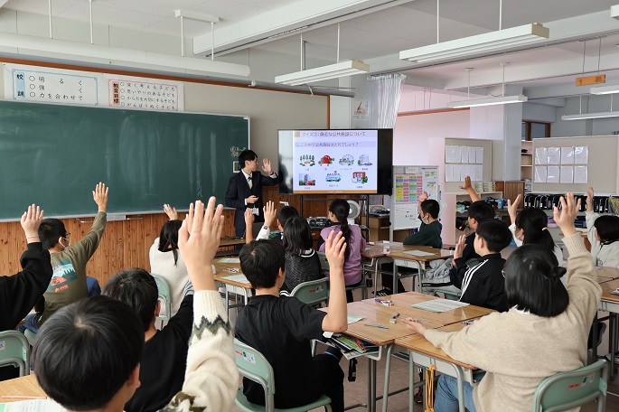 スクリーンを見ながら質問する講師と手を挙げて答える生徒達（栗沢小学校）