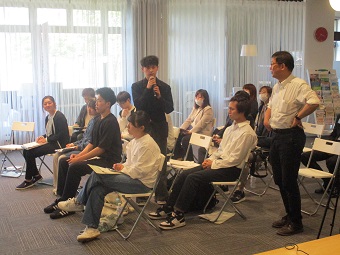 マイクを持って発表する学生とそれを聞く参加者たち