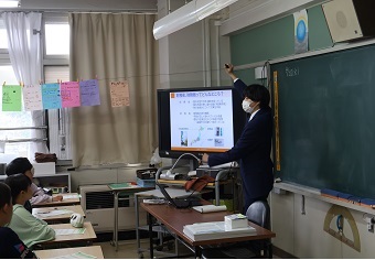 教壇で生徒たちにスクリーンに資料を映しながら財政についての講義をする講師の様子