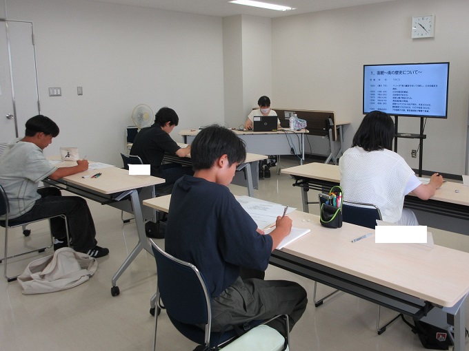 函館の歴史についてスクリーンを使って説明する講師と説明を聞く生徒