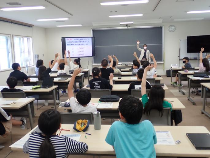 クイズを出す講師とクイズに手を挙げて回答する児童