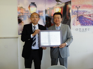 感謝状を中央に掲げている一般社団法人小樽観光協会会長と小樽出張所所長