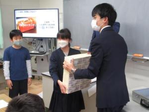 小松市立中海小学校で行われた財政教育プログラムで、お金の重さを体験するために１億円を持ち上げる児童の様子