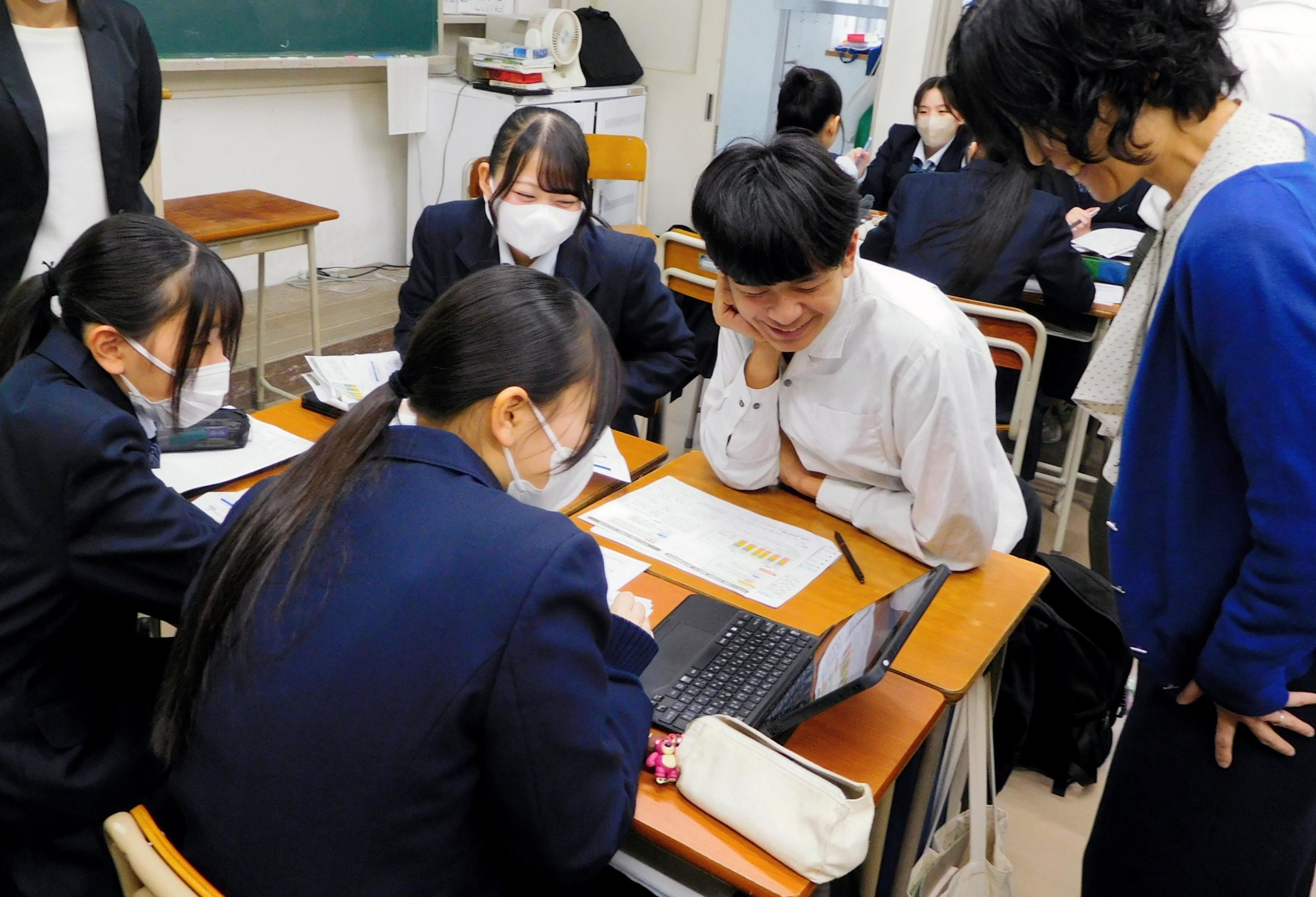 4人の高校生と担任の教諭がシミュレーションツールを見ながら笑顔で話している様子