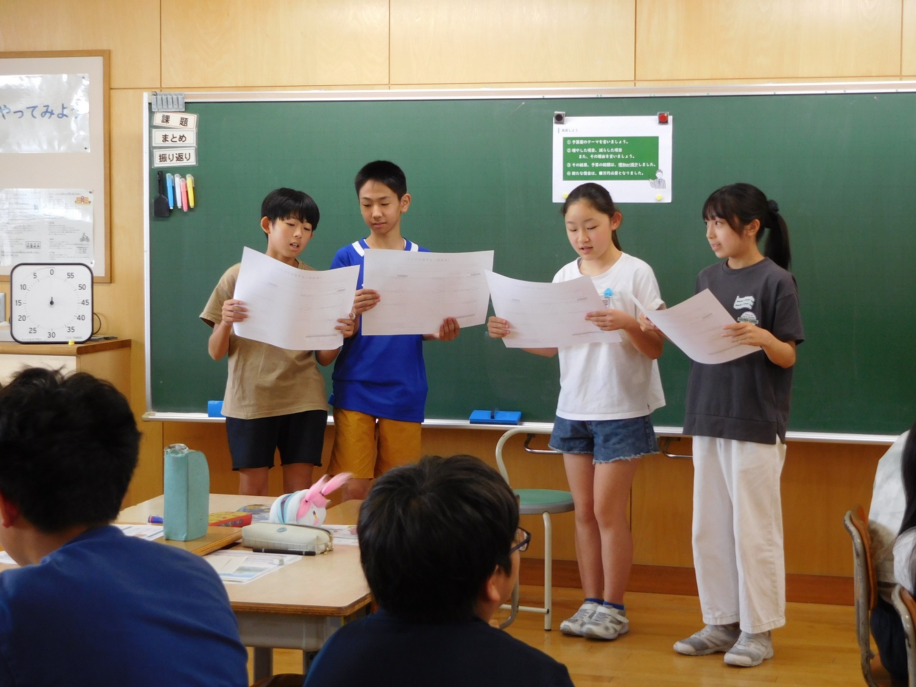 黒板の前に立った4人の児童が自分たちで考えた予算を発表している様子