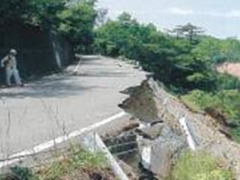災害で崩落した崖に面した道路の写真