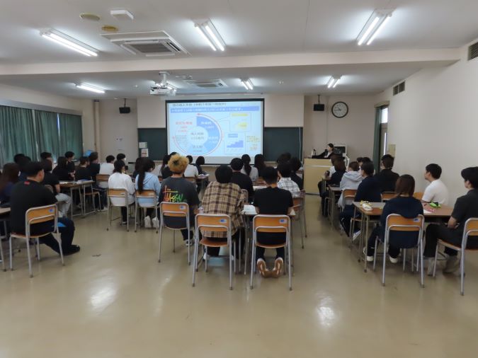 学生達が前方の講師と投影されたスライドに注目し、講義を聞いている様子