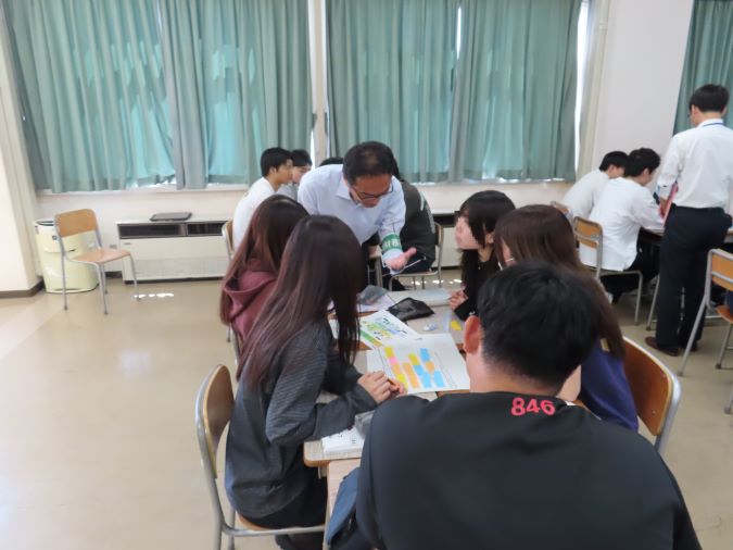 机をくっつけてグループワークをする学生が、指導員のアドバイスに聞き入る様子