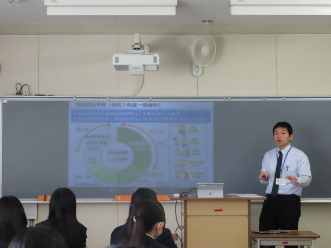 教室の黒板に資料を投影し、講師が資料を説明しながら講義を行っている様子
