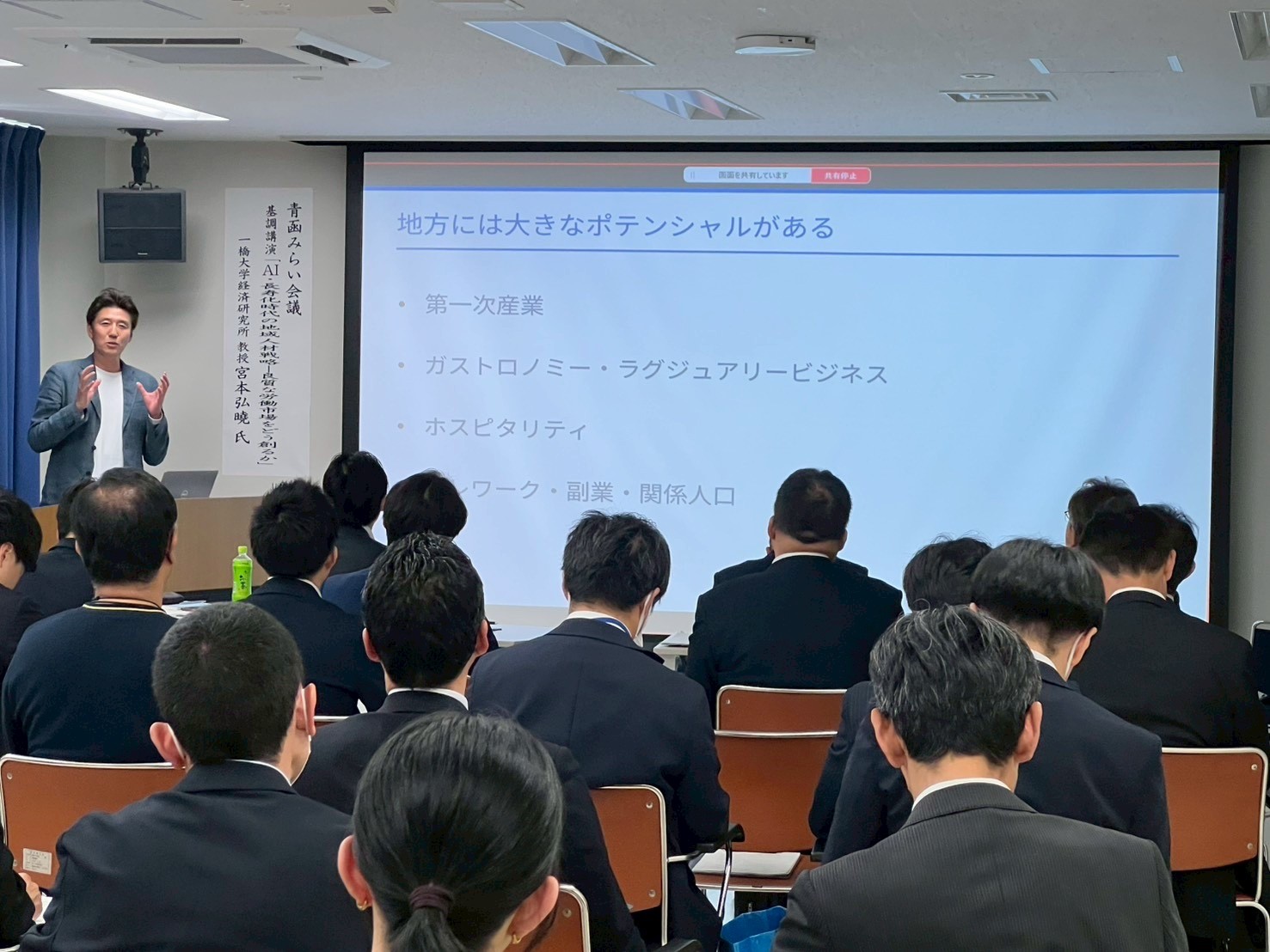 会議室でスクリーンを使い地方のポテンシャルについて説明する講演者と聴講する参加者