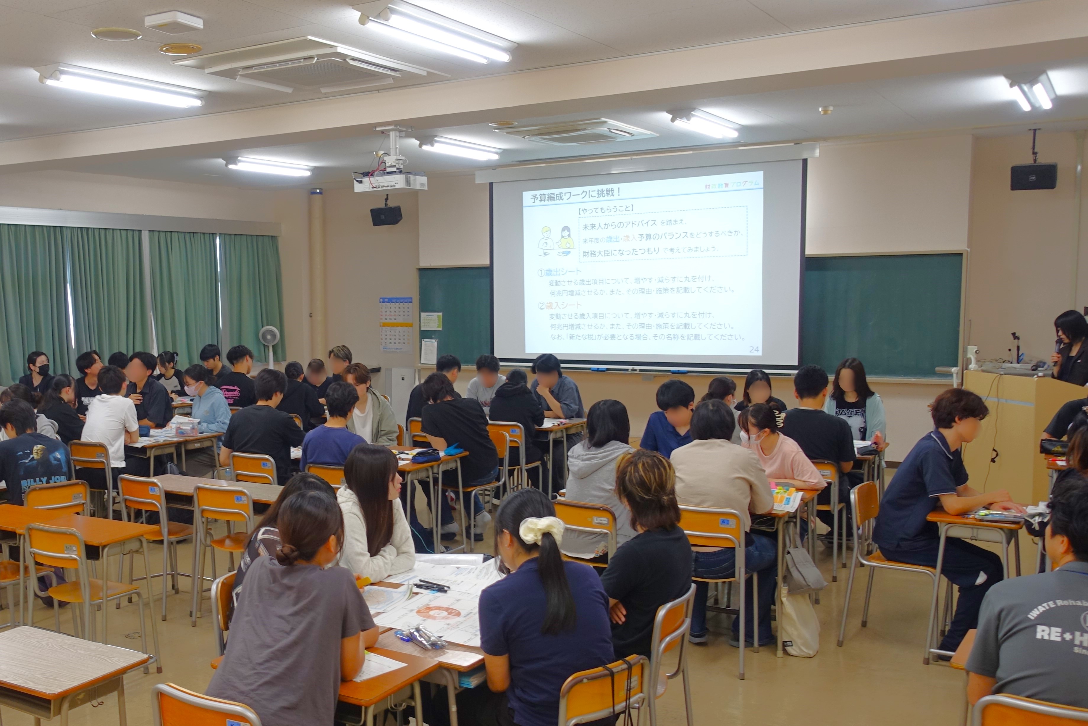 学生達が前方の講師と投影されたスライドに注目し、講義を聞いている様子
