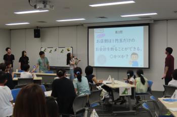 スライドに投影されたクイズを説明する東北学院大学の学生と説明を聞く参加者の様子