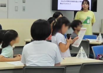 マイクをもって発表する子供と発表を聞く参加者の様子