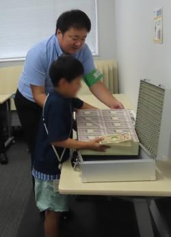 1億円の重さを体験する子供と補助する職員の様子