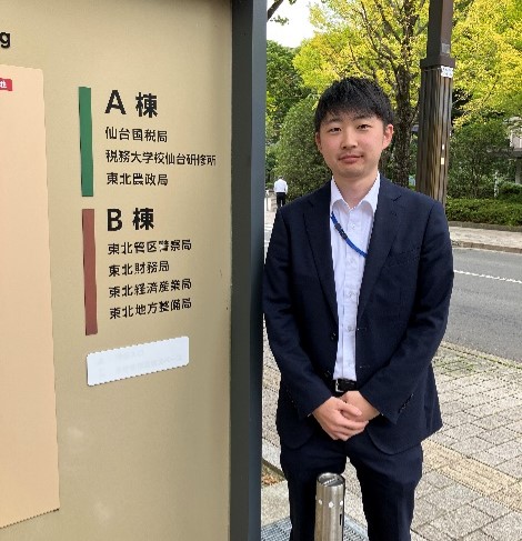 東北財務局庁舎の看板前に立つ男性職員