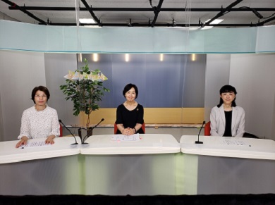 スタジオで女性アナウンサー2人の横に座っている女性職員