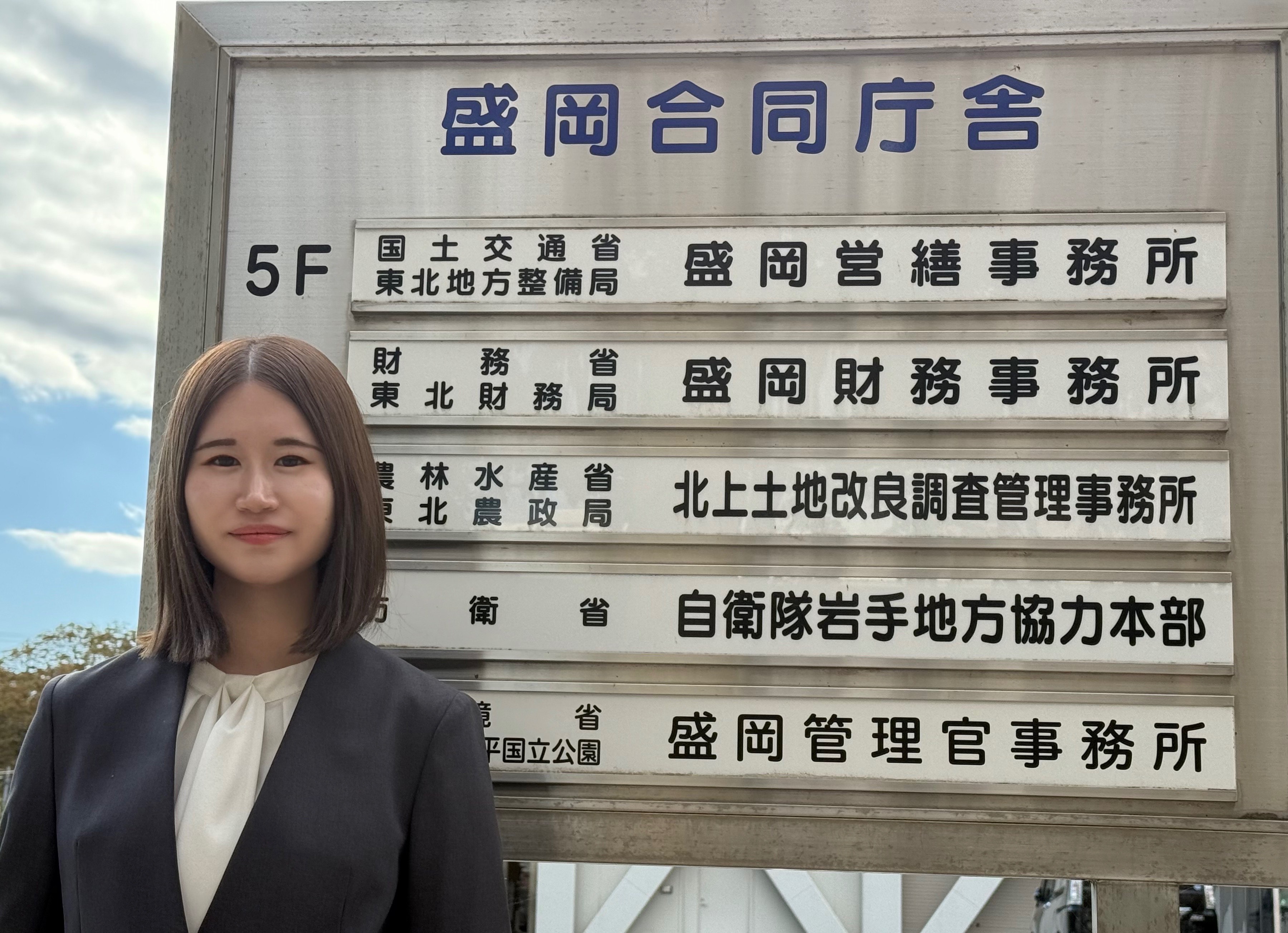 盛岡財務事務所の庁舎看板前に立つ女性職員