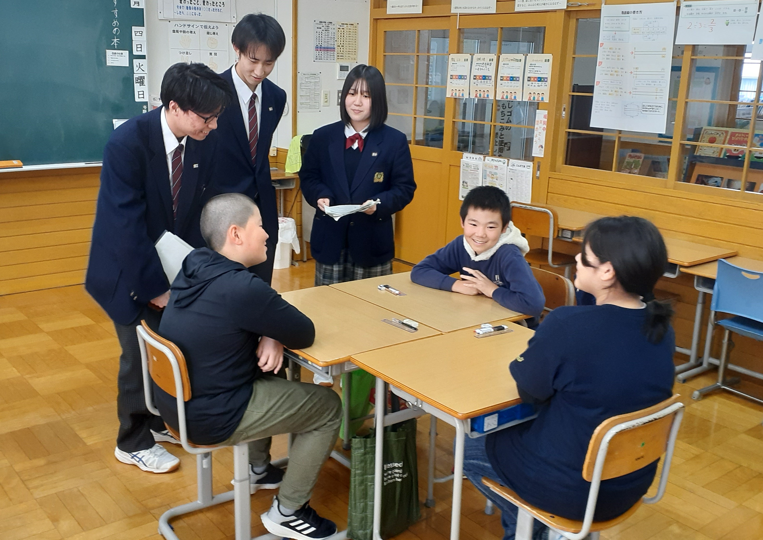 机を島にして話し合う小学生にアドバイスをする高校生