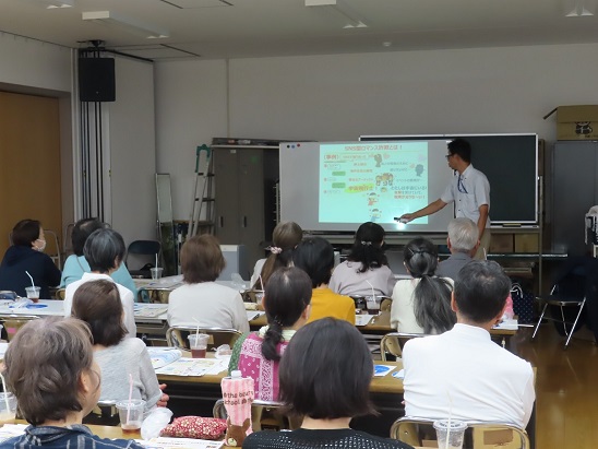 会議室で前方のスクリーンに投影された資料を見ながら講師の説明を聞いている参加者達